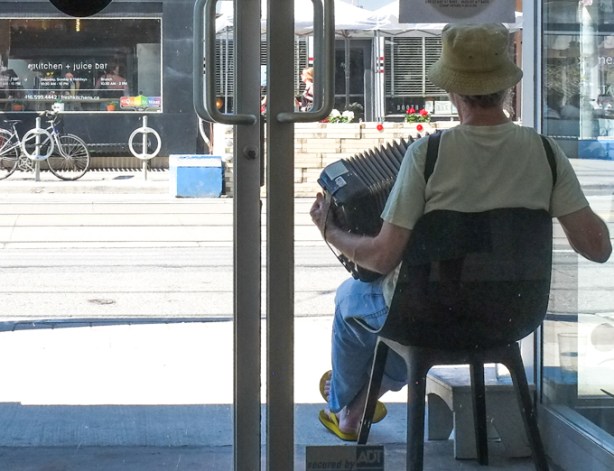 man sitting outside a glass door, playing an accordion