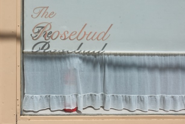 window, white curtain, words on window that say the Rosebud, shadows of the words on curtains