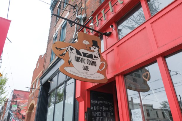 Rustic Cosmos Cafe sign with cow in a teacup. cow is wearing a black top hat and high heel shoes