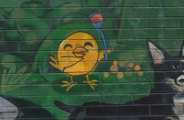 small part of animal themed mural by Uber 5000 at the Toronto Humane Society, little yellow birdie is playing fetch with a black and white dog