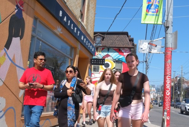 people walking on sidewalk on Queen Street West near Claremont, with mural on the Sanko Trading company in the background, the JapanTown mural