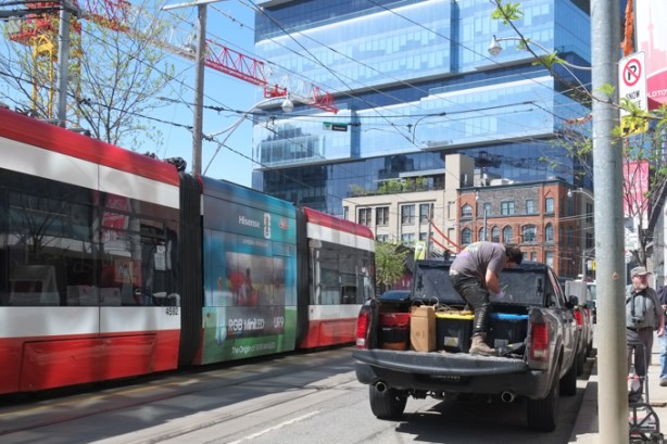 man working in back of truck on King as a TTC streetcar passes, Globe and Mail building in the background, near Ontario line subway construction