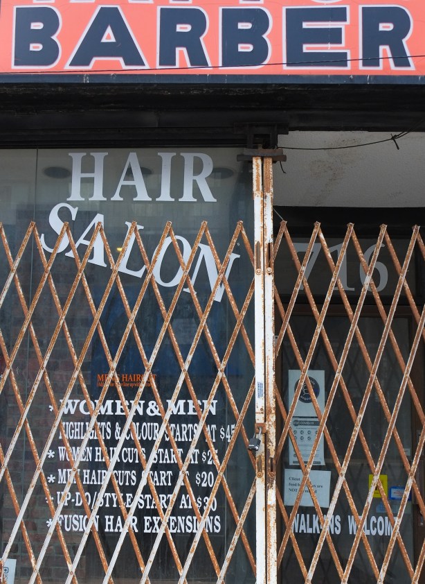 doorway of hair salon, now closed, with metal gate covering the entrance