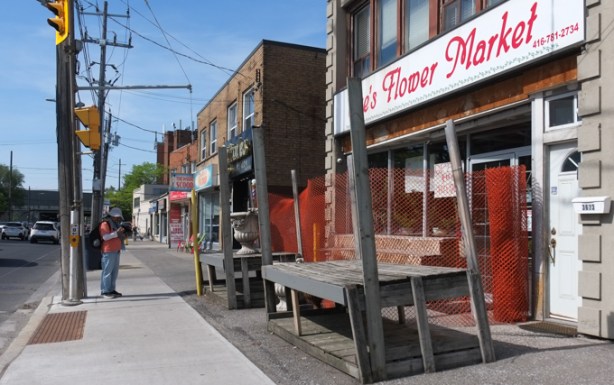 looking north up Bathurst, east side of the street, Flower Market with empty display shelves by the sidewalk, man on phone waiting for a green light