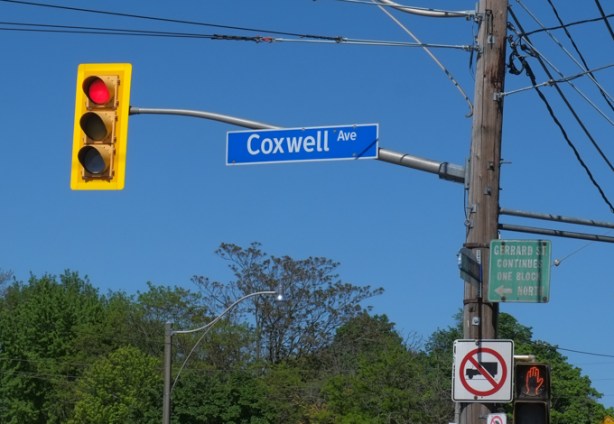 blue and white street sign, coxwell avenue, hanging by a traffic light, red light,