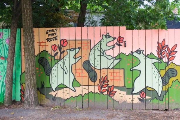mural by Emily May Rose of raccoons playing with red flowers, and sitting on brown boxes