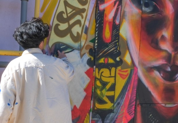 artist Rowell Soller works on a mural near Coxwell and Gerrard, a woman's face in red and orange tones