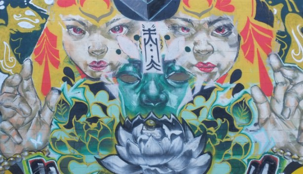 part of a mural by flips and rowell soller, 2 white faces, with a green face in the middle, yellow curvy curls