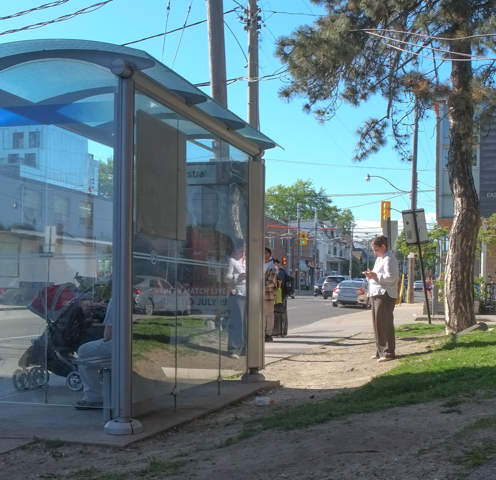 people waiting for a bus at a bus shelter on a sunny summer day