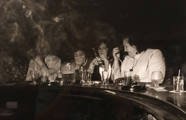 black and white photo by Larry Fink from his Social Graces series from the 1970s, women sitting at a bar smoking, with pitchers of beer on the bar