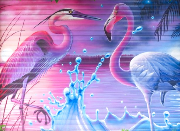 nick sweetman mural on a garage door in pinks and blue, pelican on the pink side, flamingo on the blue, water bubbles splashing in the middle