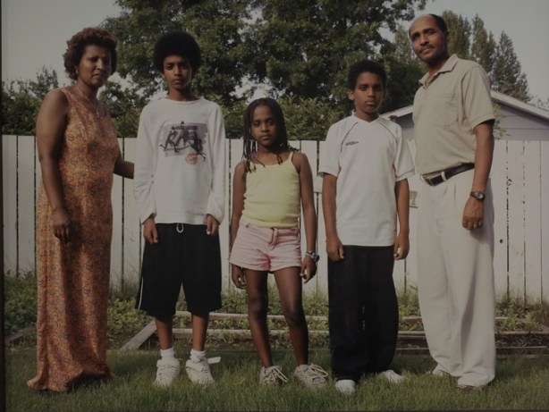 photo by Dawit Petros in art gallery, colour photo, family portrait, 5 people standing in a line, parents at the ends, three kids in the middle with shortest daughter in the very center