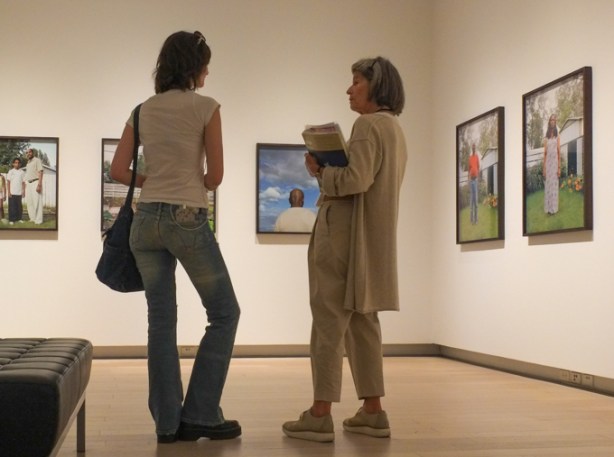 two women talking while standing looking at photographs, family photos in colour by Dawit Petros in art gallery