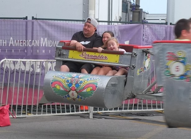 father and two girls on scrambler midway ride, father looking bored, girls looking excited