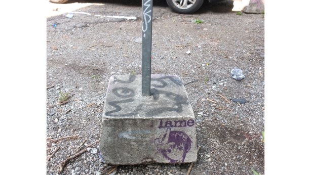 concrete block at the base of a sign on a metal pole, stencil graffiti on the concrete that says lame