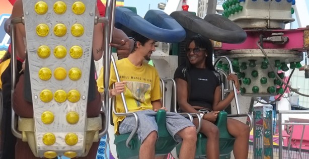 two people seated, waiting for a ride to start, talking to each other and smiling