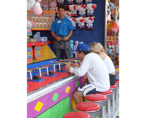 game at CNE midway, shooting water at a target to win a stuffed animal, two people seated on red stools to play the game