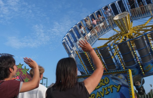 people waving to others who are on the zero gravity ride at the ex midway