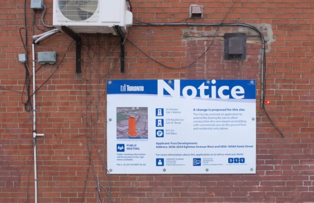 blue and white redevelopment notice sign on the side of a red brick building