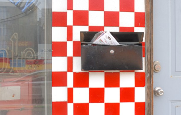 black mailbox on wall with red and white tiles in checkerboard pattern