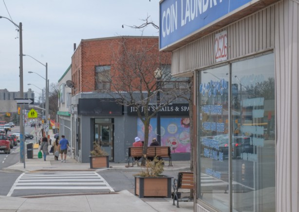 in front of a coin laundry, northside of Eglinton Ave., looking west towards Keele, people sitting on a bench outside nails and spa shop, other people walking on sidewalk