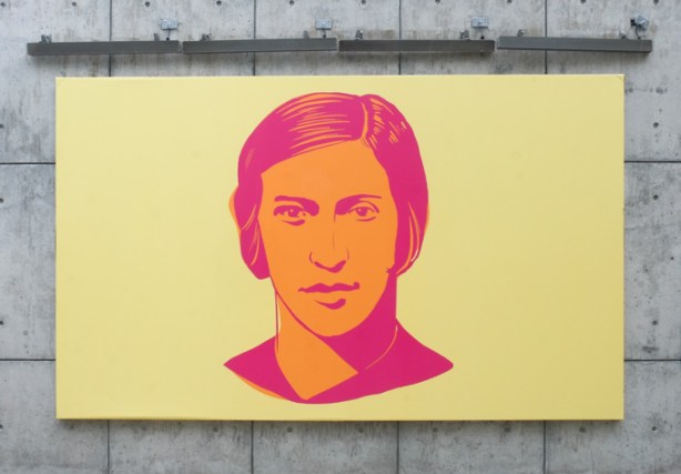 outdoor mural, portrait of Fanny Bobbie Rosenfeld in orange and pink on yellow background. mounted on wall made of concrete
