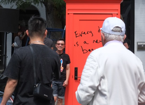 a young man stands in front of an orange door with writing on it that says every day is a new beginning, posing for a photograph, door is part of interactive art display