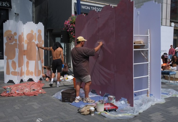 man painting a large section of temporary wall in maroon colour in prep for a mural painting