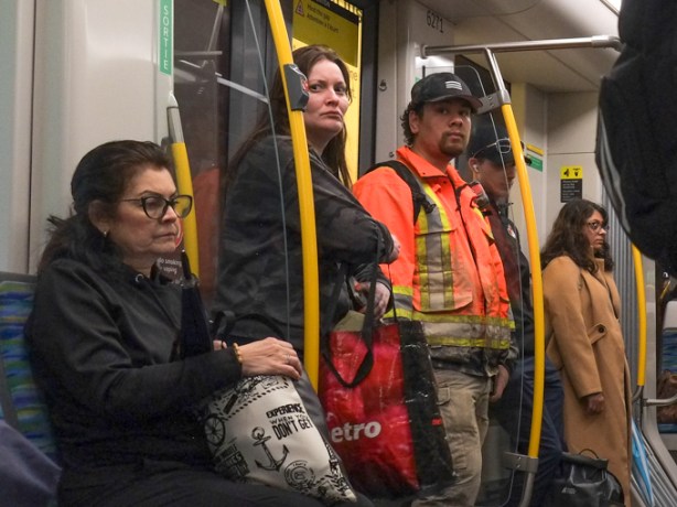 people on an LRT train, TTC, 4 people standing and one woman seated