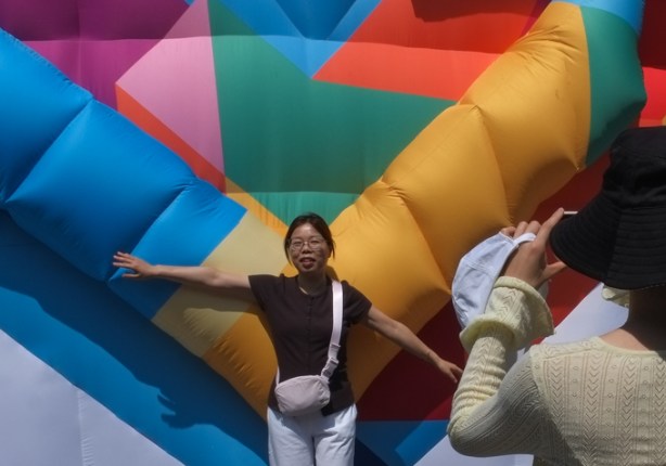 asian woman posing for a picture beside a large multi coloured inflatable heart, public art display