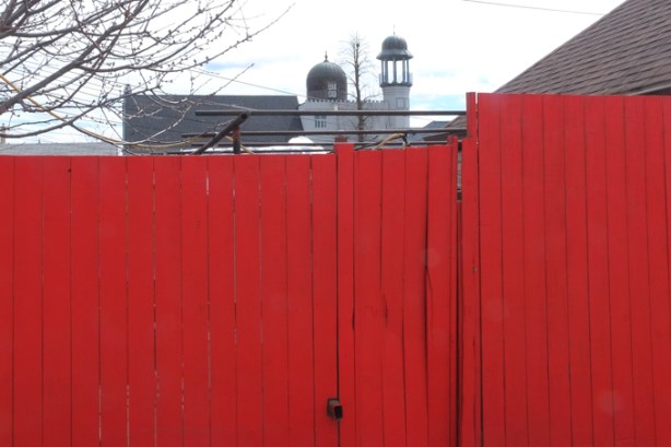 bright red wood fence with top of mosque just showing over the fence