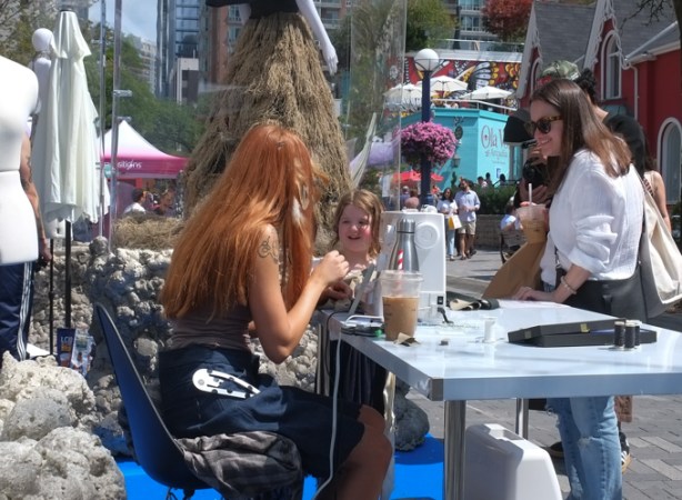 mother and daughter watching a woman at a sewing machine, outdoors, Yorkville