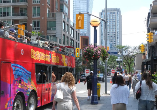 open top tourist bus, hop on hop off, in Yorkville with people on the sidewalk beside it
