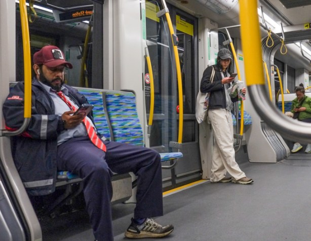 two people on an LRT train, one is a young man standing by the door, the other is a TTC employee in uniform, sitting