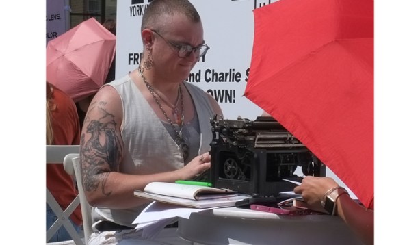 a person with shaved head, and many tattoos on arm, dangling earrings, and a couple of necklaces, at an old fashioned typewriter, typing poetry, outdoors, 