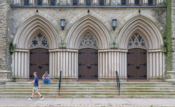 man sitting on steps of St. Pauls church, wide steps, three doors, another man walks past
