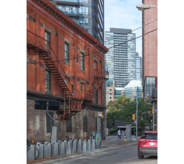older three storey red brick building on Howard Street, with newer buildings in the background, a red car on the street