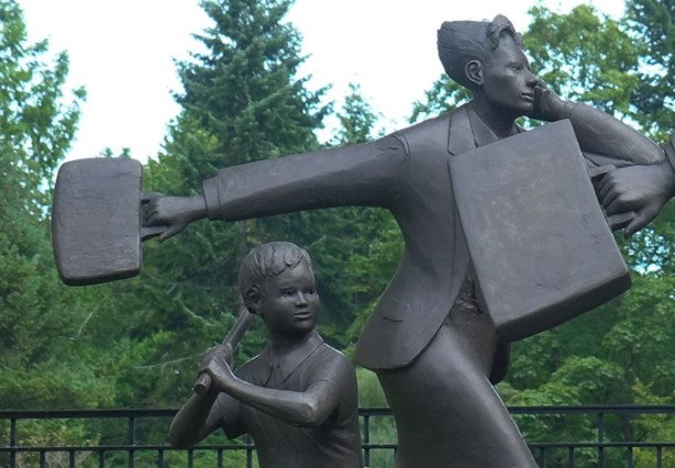 part of sculpture titled community, by Kirk Newman, life sized people going about their day, woman carrying briefcase, boy with a baseball bat