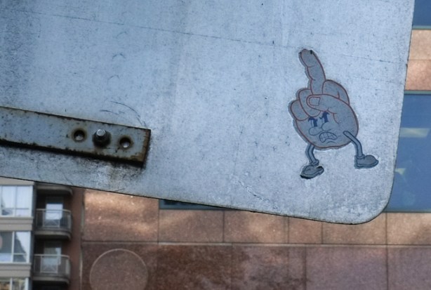 graffiti on the back of a city sign that is a growling character made of a hand giving the figure