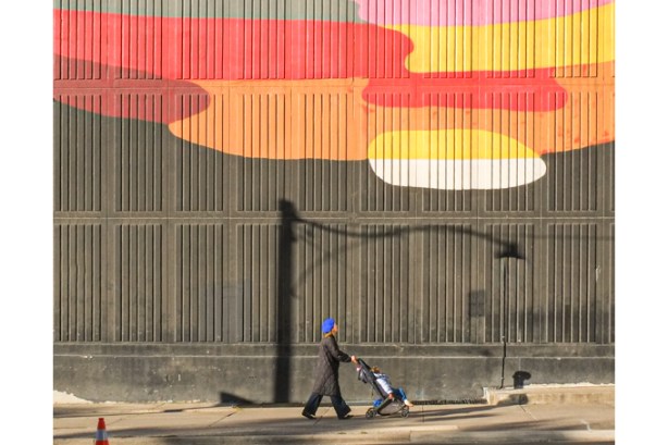 woman pushing a stroller past the bottom part of mural, Equilibrium, by Okuda San Miguel 